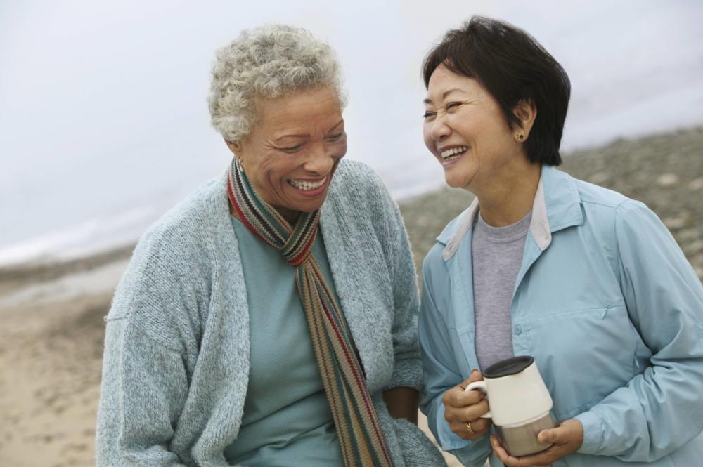 two women laughing while on walk on a beach